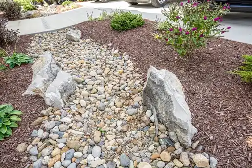 Rock and mulch landscape bed with plants, a water fountain, and large boulders as the perimeter