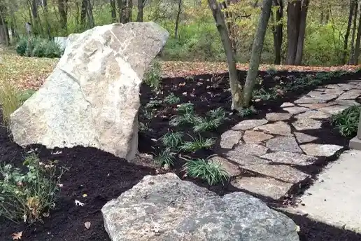 Side view of mulch, paver rock walkway, and large boulder landscaping